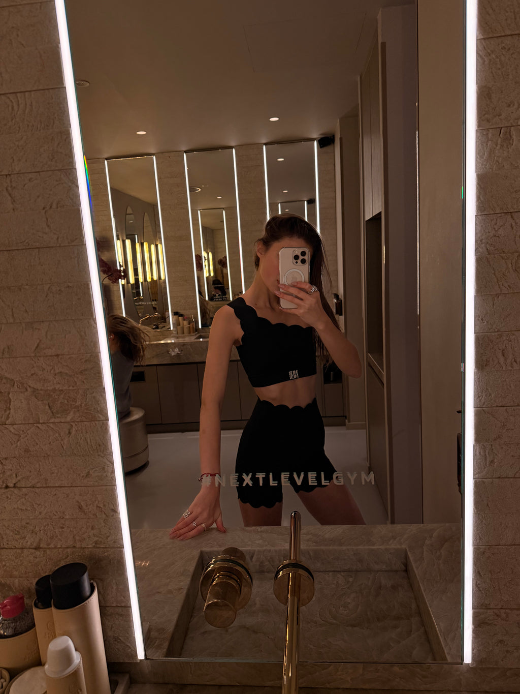 Person taking a mirror selfie in a bathroom with a lit mirror.